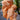 Peach Crinkle Chile peppers, with peach-colored, wrinkled skin and pointed tips, cluster on a green plant against blurred leaves and a tiled floor, hinting at the spicy seeds inside.